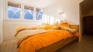 Una camera da letto con un letto di legno, pareti bianche, una finestra vista montagna e un termosifone.
