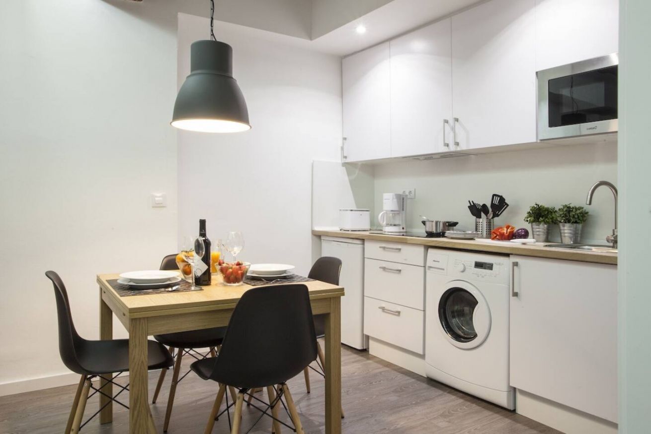 Et moderne køkken med hvide skabe, en indbygget vaskemaskine og et spiseområde med bord og stole.