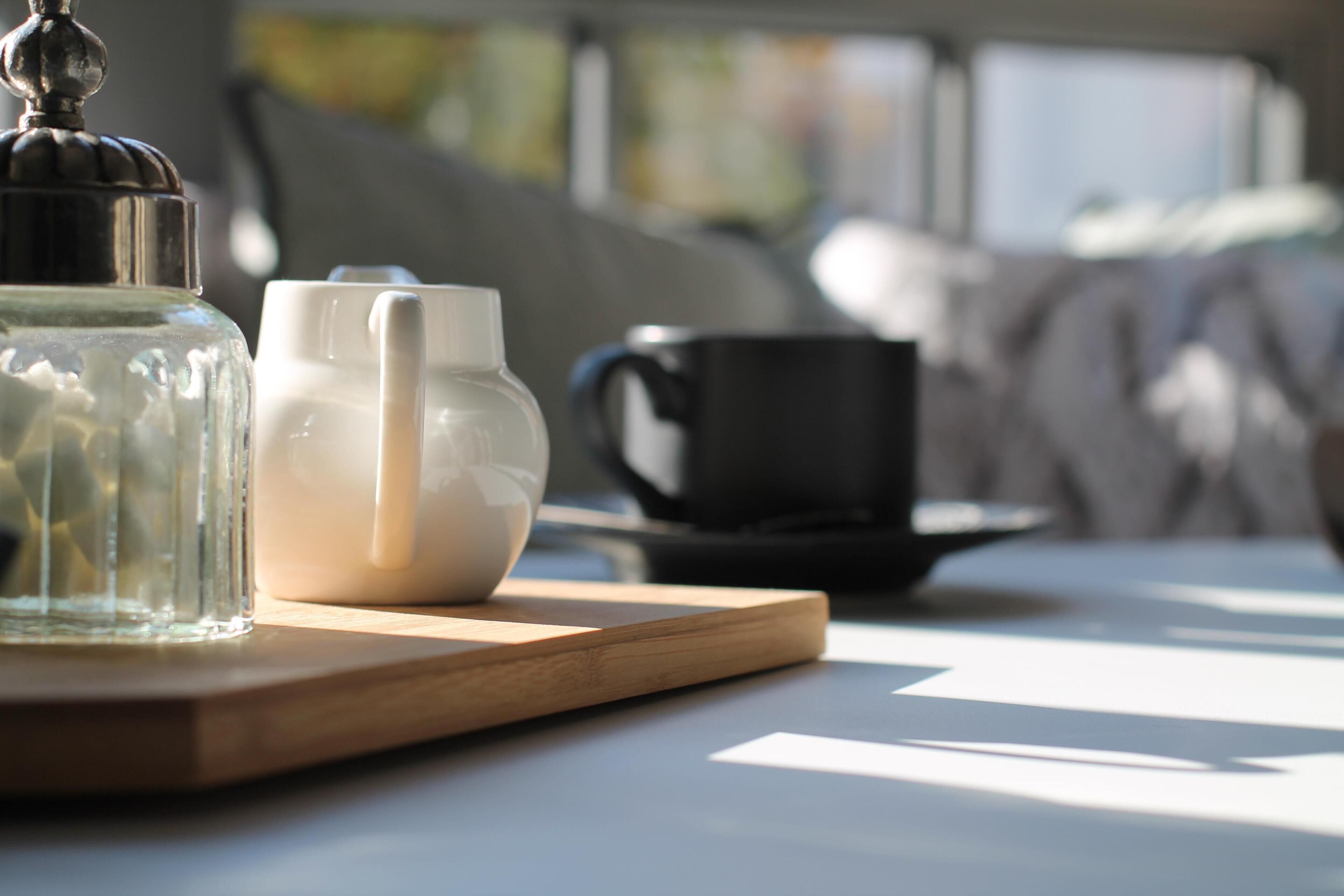 A clear glass container, a white ceramic pitcher, and a black mug on a wooden tray.