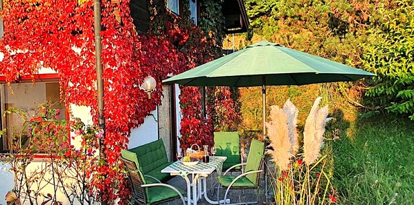 Un espace extérieur aménagé avec une table et des chaises, entouré de feuillage rouge et de plumes d’herbe des pampas.