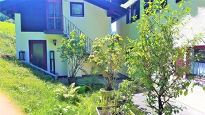 Une maison à deux étages avec un balcon, un escalier et un jardin où poussent différentes espèces de plantes.