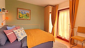 Une chambre à coucher avec un lit, une chaise, un tableau et une fenêtre avec des rideaux.