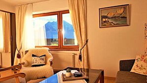 Une pièce chaleureuse avec vue sur les montagnes, un fauteuil moelleux, une table avec une plante et un tableau accroché au mur.