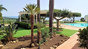 Zona de piscina amb una pèrgola, palmeres i vista al mar.