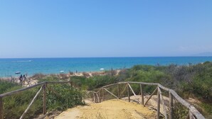 Unes escales de fusta que condueixen a una platja amb una vista clara del mar i muntanyes llunyanes.