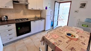Cuina senzilla amb fornet a gas, rentapeus i armaris moderns. Al primer pla, una taula de dinar amb mantell estampat.