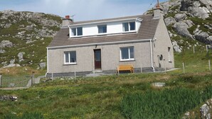 Une maison à deux étages, dotée d’un toit en pente, d’une porte d’entrée et d’un petit porche avec un banc.