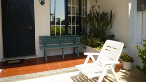 A patio with a white chair, a green bench, and potted plants.