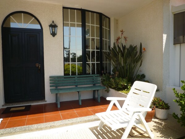 A patio with a white chair, a green bench, and potted plants.