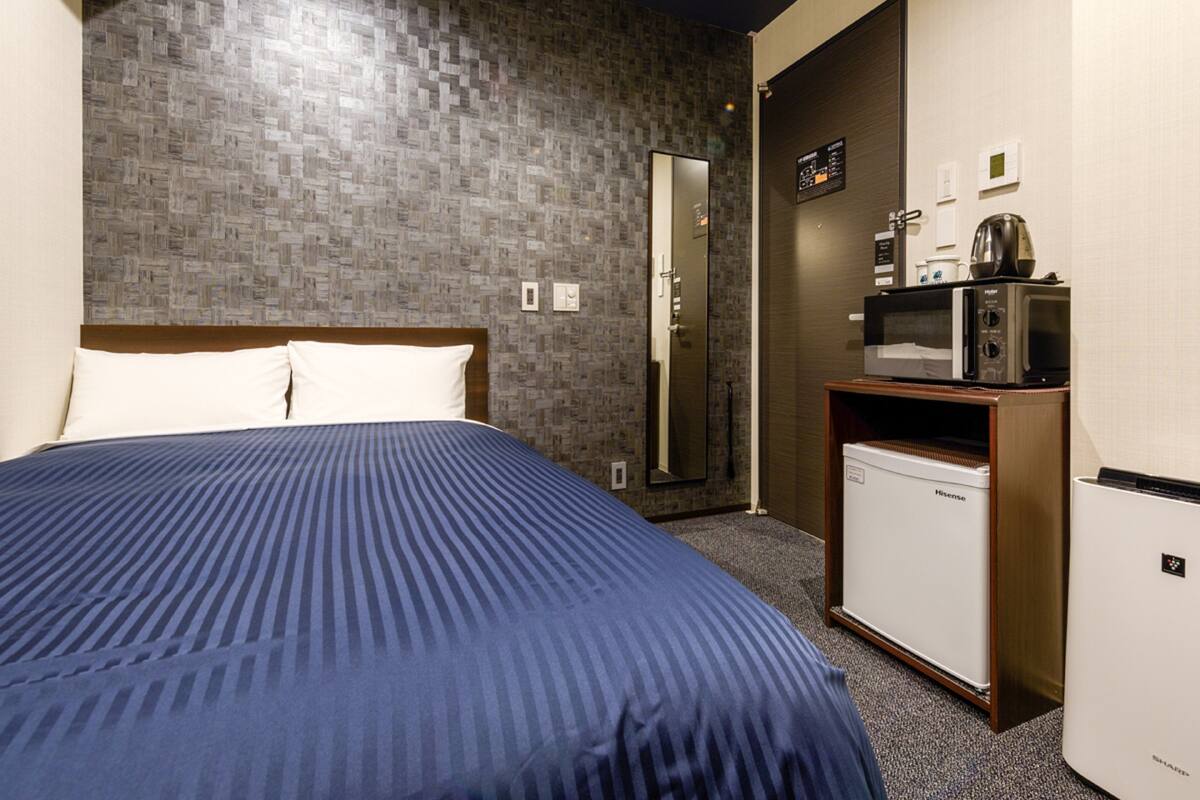 A hotel room with a bed, a refrigerator, a microwave, and a small kitchenette.