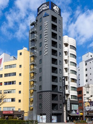 Un hôtel moderne, avec plusieurs étages, des balcons et une enseigne bien visible indiquant « HÔTEL LIVESMAX ».