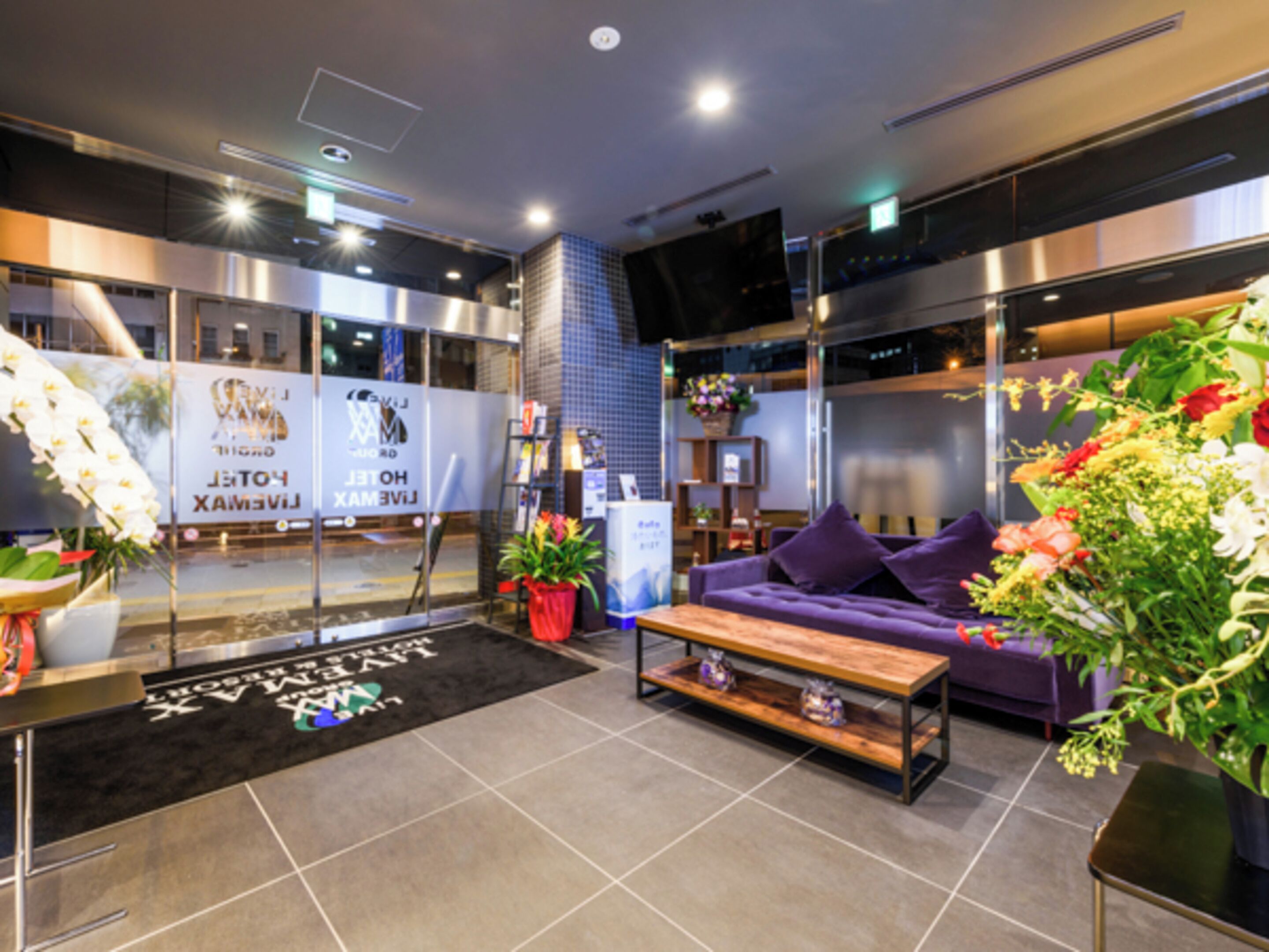 A modern hotel lobby with a sofa, coffee table, potted plants, and a reception desk.