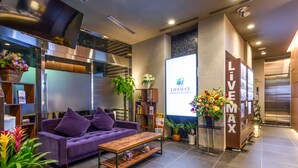 A modern hotel lobby with a purple sofa, a wooden coffee table, and a large screen displaying the hotel name. - Hotel Livemax Asakusabashi Station (Tokyo)