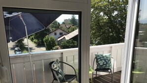 A balcony with a chair and an umbrella, overlooking a street with houses and cars.