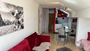 A compact living space with a red sofa, a dining area with a table and chairs, and a kitchen area.