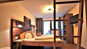 A bedroom with a wooden bed, a nightstand, a lamp, and a view of the outdoors through a window.