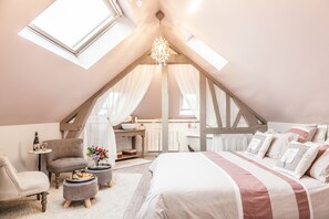 Une chambre confortable avec un plafond en pente, un lit avec une literie à rayures, une petite table ronde, une chaise et une coiffeuse avec un miroir.