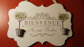 Een decoratief welkombord met de tekst 'BIENVENUE Au petit Bonheur' en twee kleine planten in potten.