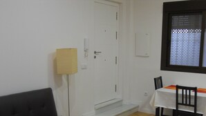 A room with a black sofa, a small table with two chairs, a white door, and a window with a patterned blind. - Nice loft in downtown Seville (Sevilla)