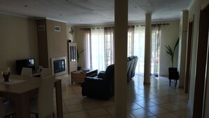 Un vaste salon doté d’une cheminée, d’un téléviseur, d’un coin repas et d’un espace détente avec un canapé et des fauteuils.