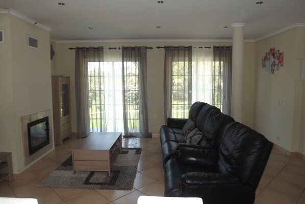 A living room with a black leather sofa, a wooden coffee table, a TV, and a fireplace. - 3 bedroom single storey house, close to all services (albufeira)
