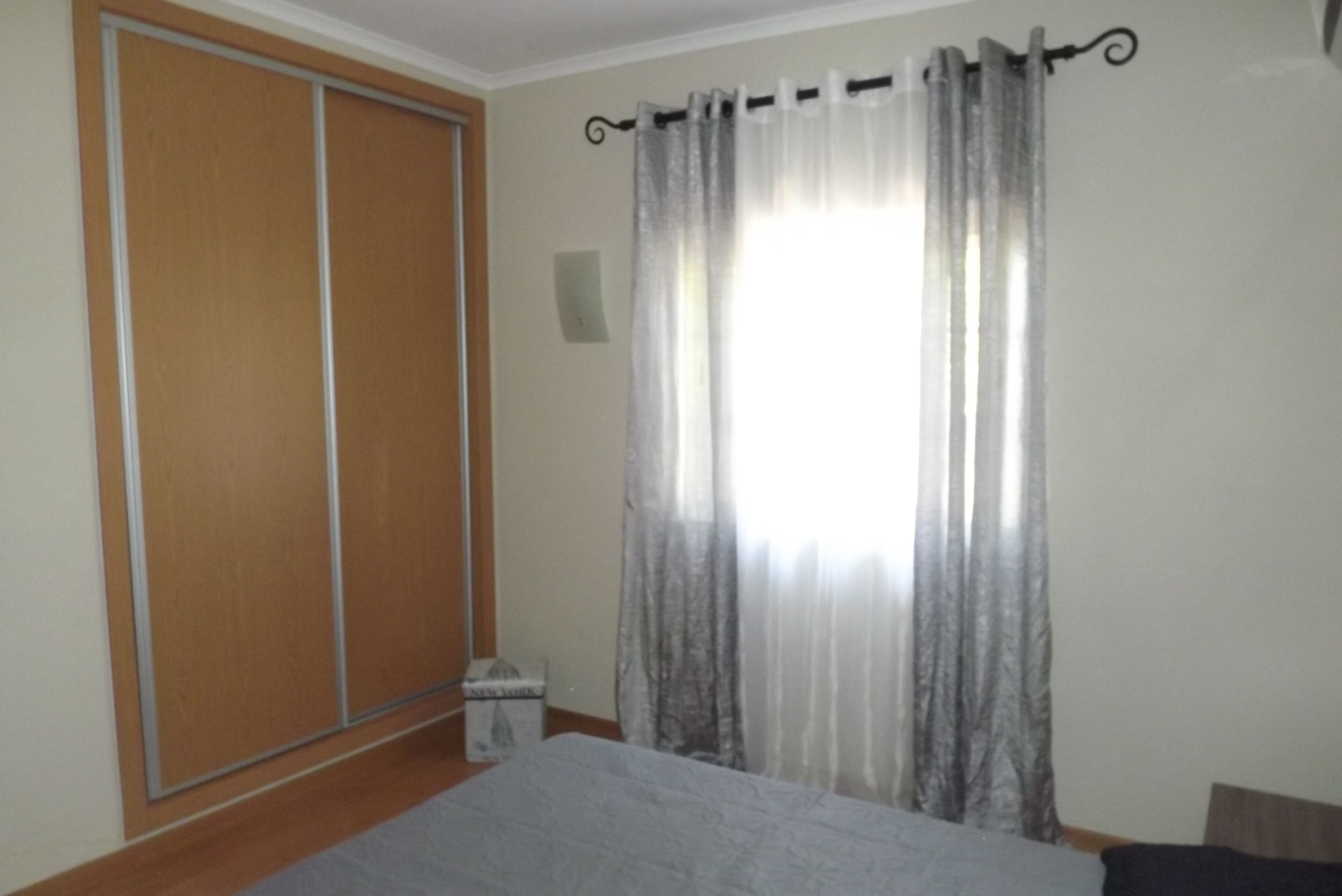 A bedroom with a bed, a wardrobe, and a window with curtains.