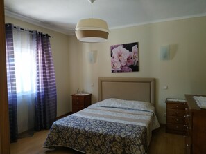 A bedroom with a bed, a nightstand, a dresser, a ceiling light, and a wall-mounted picture of flowers. - 3 bedroom single storey house, close to all services (albufeira)
