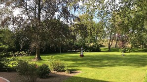 Ein gepflegter Park mit Rasenfläche, Bäumen und einer kleinen Statue eines Segelboots.