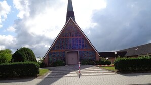 Eine Kirche mit einem Spitzspitzboden, großen Buntglasfenstern und einer Ziegel-Fassade.