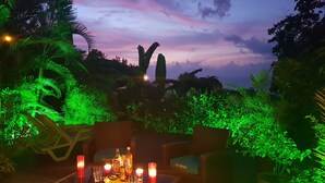 An outdoor dining area with wicker furniture and candles, surrounded by lush greenery and a view of the sky. - CocosunLodge * superb sea view and private pool * (TROIS ILETS)