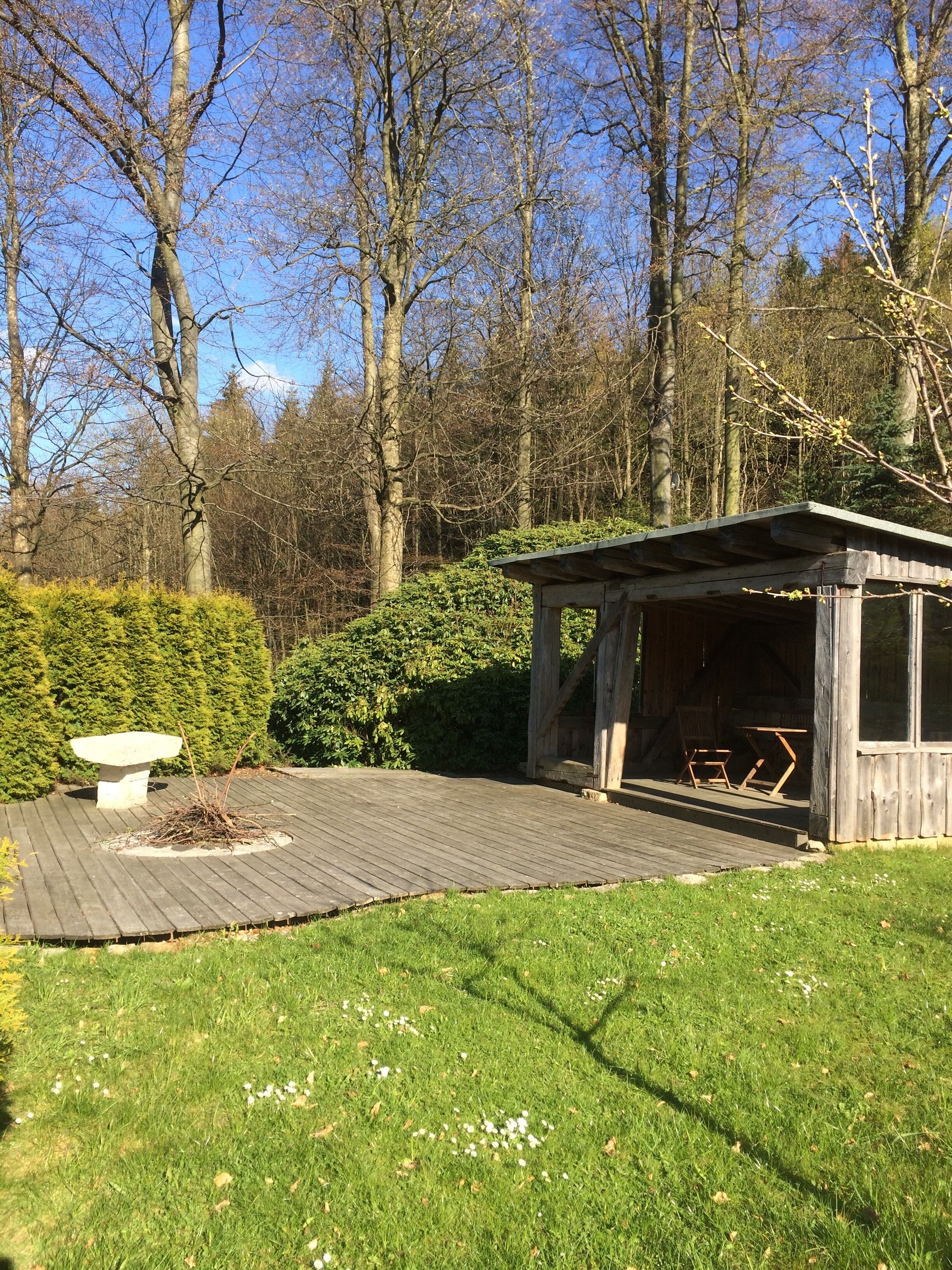 A wooden gazebo with a bench, surrounded by a grassy area and dense shrubbery.
