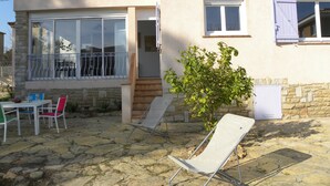 A house with a stone facade, a balcony with metal railings, and a small garden area with a chair and a table.