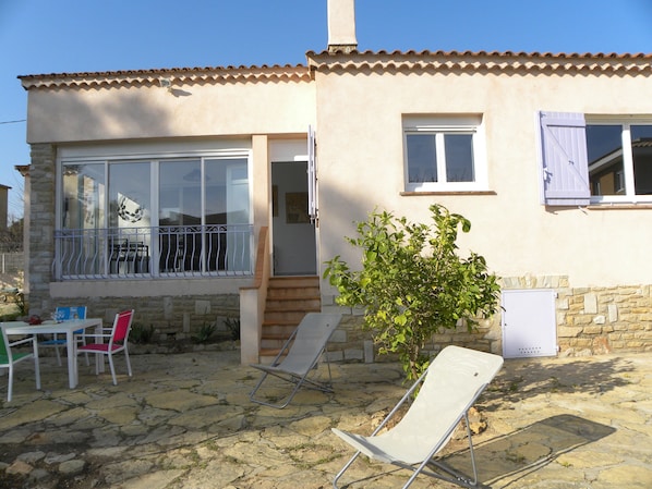 A house with a stone facade, a balcony with metal railings, and a small garden area with a chair and a table.