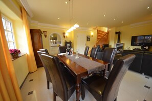 Een eetgedeelte met een houten tafel en stoelen, een keuken op de achtergrond, en een trap die naar een andere verdieping leidt.