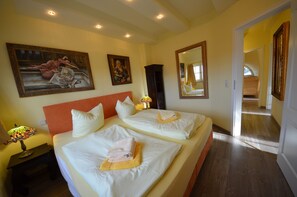 Een hotelkamer met twee bedden, een groot schilderij aan de muur, een spiegel en een gang naar een andere kamer.