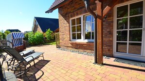 Et murstenshus med et stort vindue, en overdækket terrasse med udendørs møbler og en blå markise.
