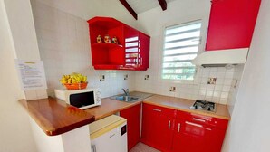 A compact kitchen with a microwave, sink, and red cabinets. - A rejuvenating stay in our peaceful gîtes (SAINTE ROSE)