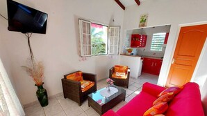 A living room with a red sofa, two wicker chairs, a coffee table, and a TV mounted on the wall. - A rejuvenating stay in our peaceful gîtes (SAINTE ROSE)