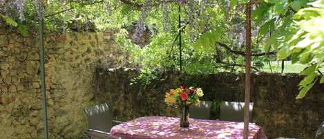 An outdoor patio with a table set for two, surrounded by chairs, and a vase with flowers on the table.