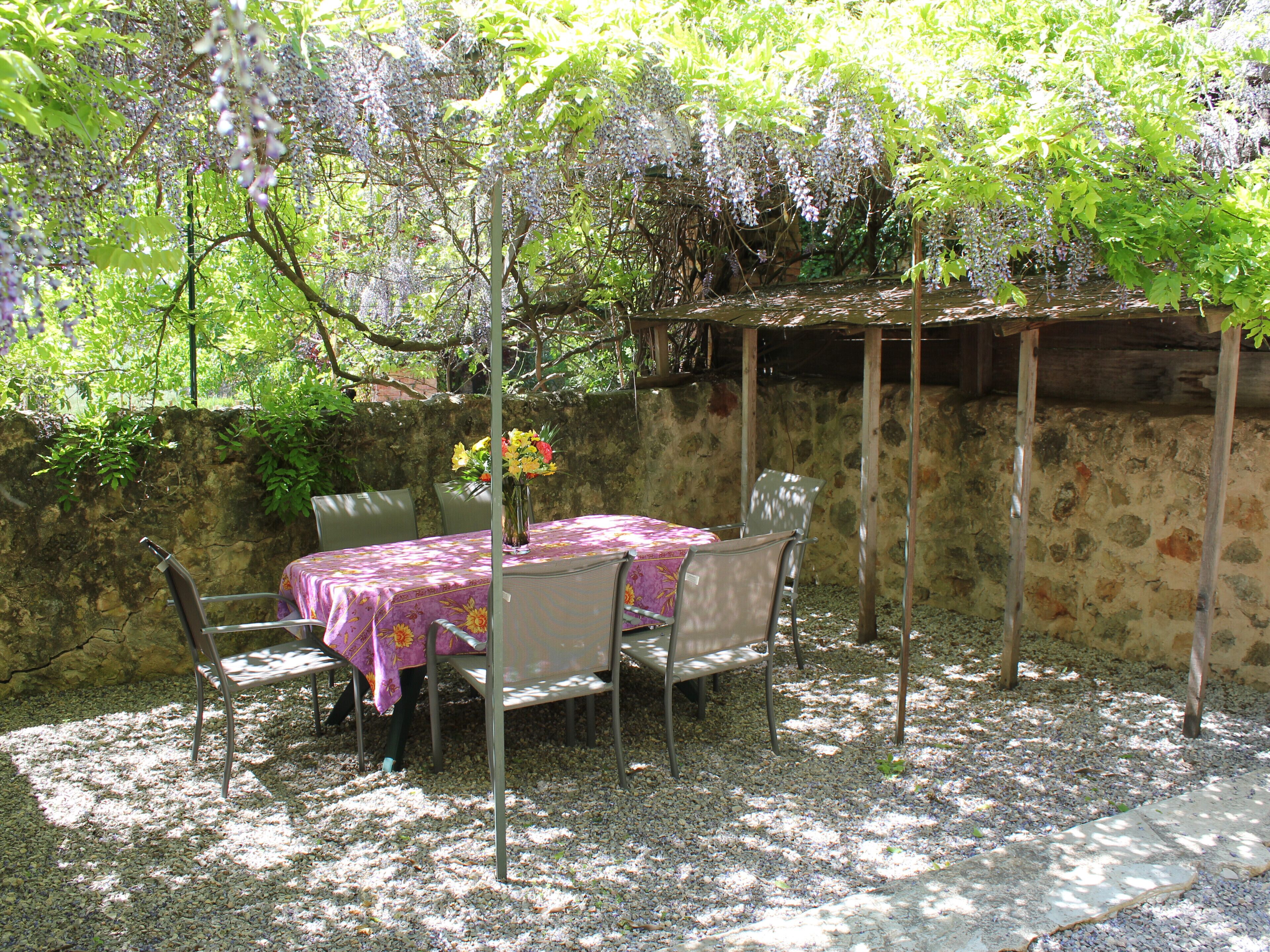 Eine Terrasse im Freien mit Tisch und Stühlen, umgeben von einer Steinmauer und üppiger Bepflanzung.