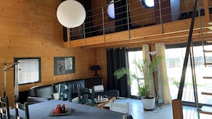 A spacious room with a high ceiling, wooden beams, a dining area with a table and chairs, a sofa, and a large potted plant.