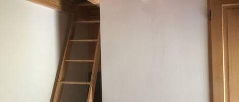 Ein Zimmer mit einer Holzleiter an einer weißen Wand, einer Holztür und einer geneigten Decke mit freiliegenden Balken.