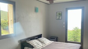 A bedroom with a bed, a ceiling fan, a window, and a door. - F3 of 80m ², swimming pool with sight on sea and mountains Arrival possible during the week (Calcatoggio)