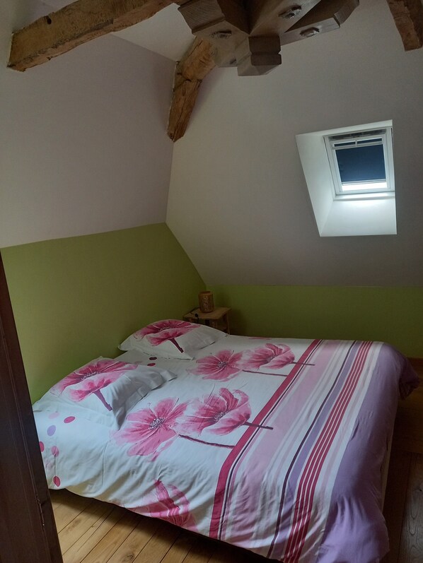 Une chambre avec un lit, une petite fenêtre et une poutre en bois au plafond.