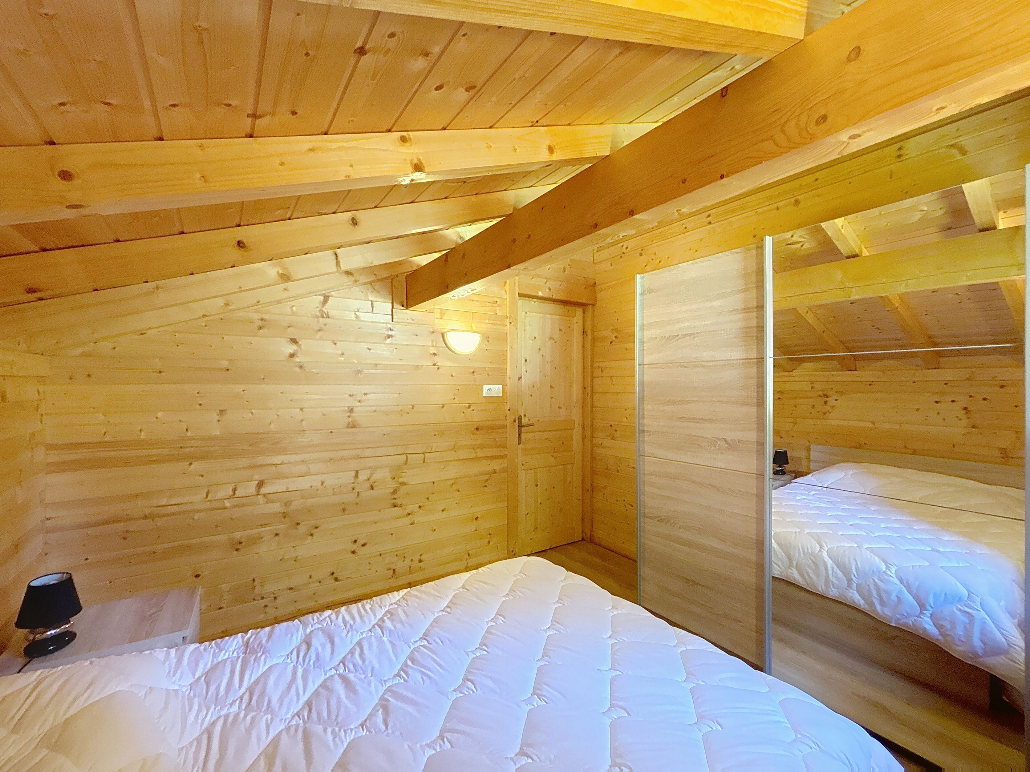 Une chambre dans un chalet en bois, avec un lit superposé, une table de chevet avec une lampe et une petite fenêtre.