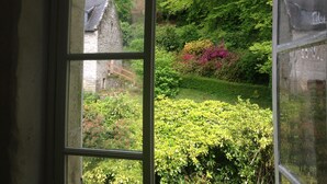 Udsigt gennem et vindue af en bygning i sten omgivet af frodig vegetation og blomstrende planter.