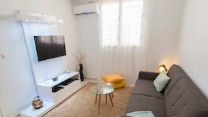 Un soggiorno moderno con un divano grigio, un tavolino rotondo, una poltrona grigia, una TV a schermo piatto montata su una parete bianca e un tappeto beige.