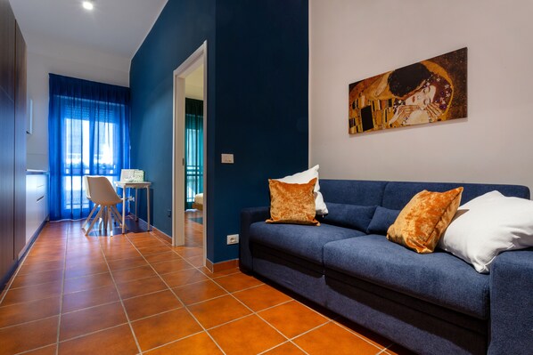 Un salón moderno con un sofá azul, dos cojines y un cuadro en la pared.