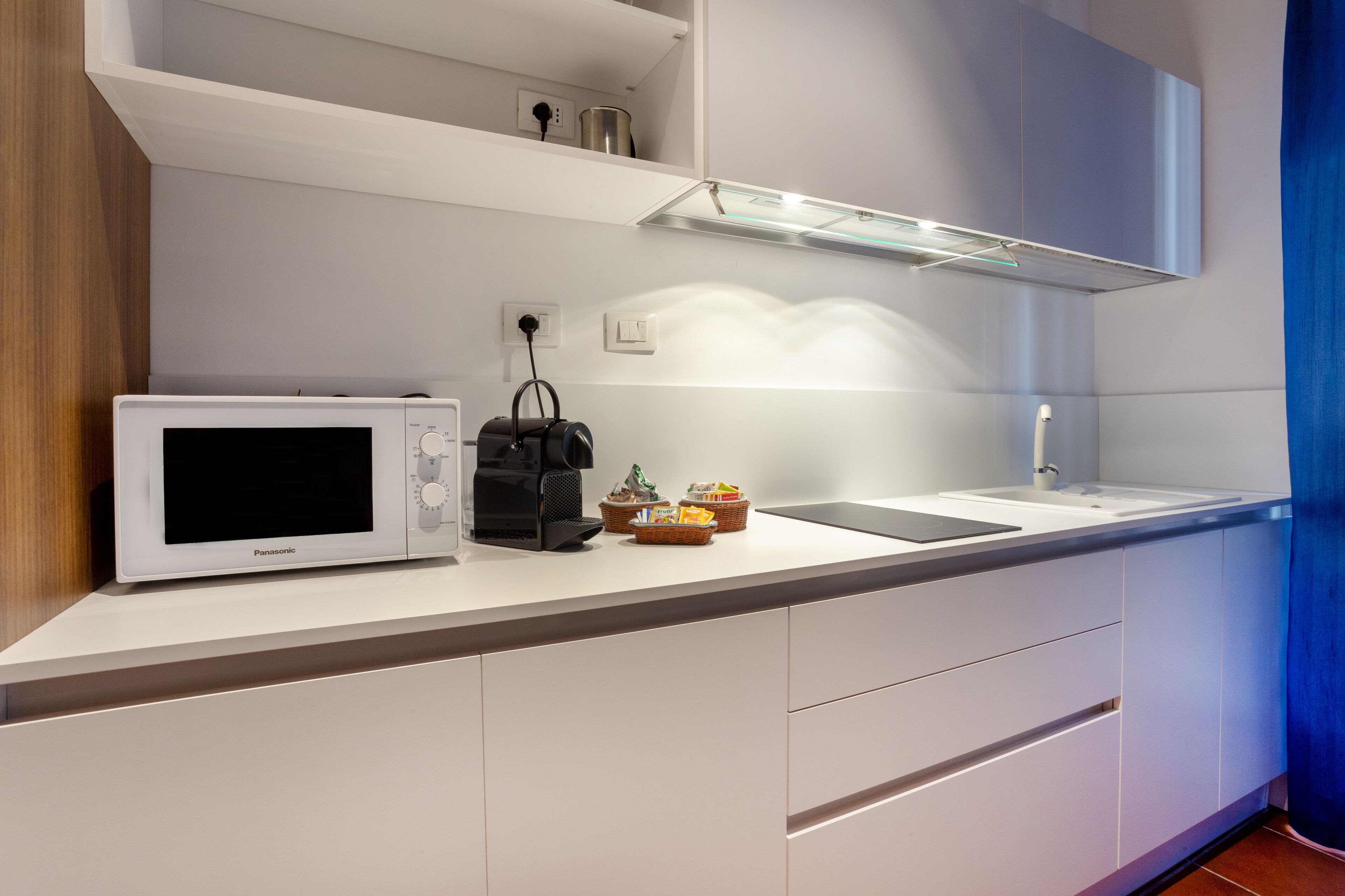 Een moderne keuken met witte kasten, een wit aanrecht, een magnetron, een koffiezetapparaat en een spoelbak.