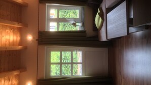 A room with a wooden interior, a window with a view of greenery, and a light fixture on the wall. - Guest house "Living in the garden of the senses" (Kindenheim)